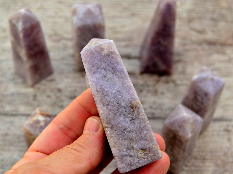 One lepidolite tower stone 85mm on hand with background with some obelisks on wood table