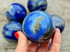 One blue lapis lazuli crystal sphere 55mm on hand with background with some lapis balls on wood table