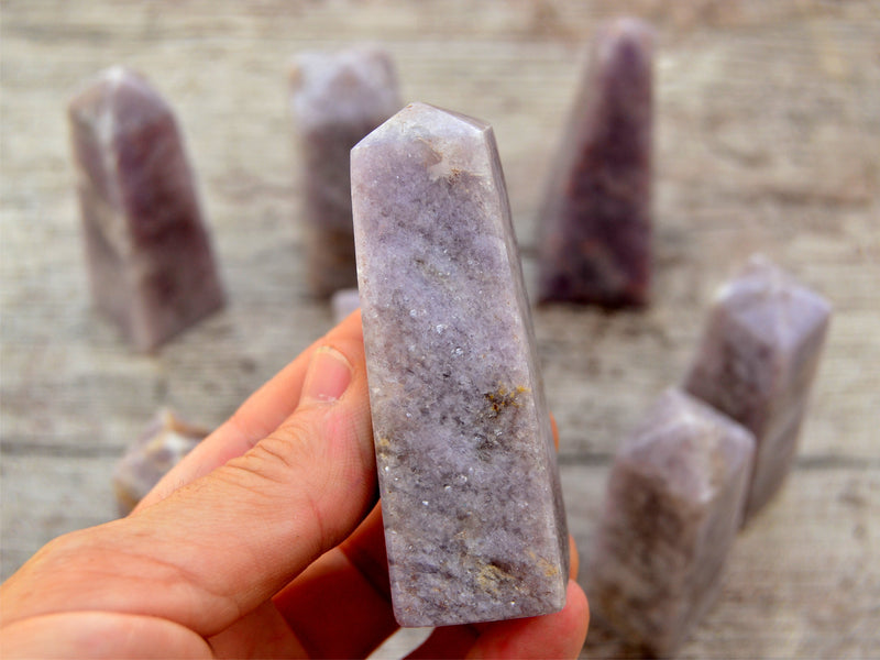 One lepidolite tower stone 80mm on hand with background with some obelisks on wood table