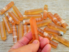 One small honey calcite crystal point 55mm onhand with background with several crystals on wood table