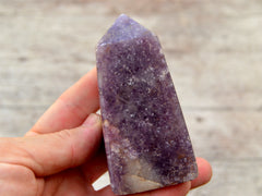 One chunky purple lepidolite tower 90mm on hand with background with wood background