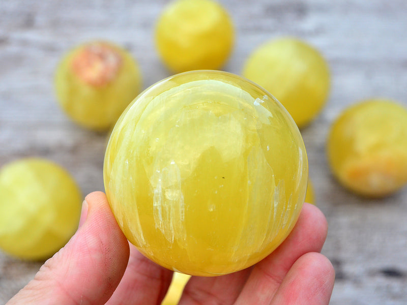 One lemon yellow calcite sphere crystal 50mm on hand with background with some stones on wood table