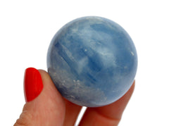 One blue calcite crystal sphere 25mm on hand with white background