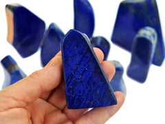 Blue lapis free form slab crystal on hand with background with some stones on white