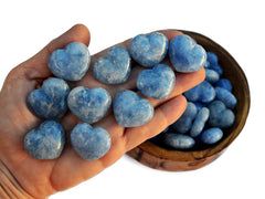 Ten mini blue calcite hearts 30mm on hand with background with some stones inside a wood bowl