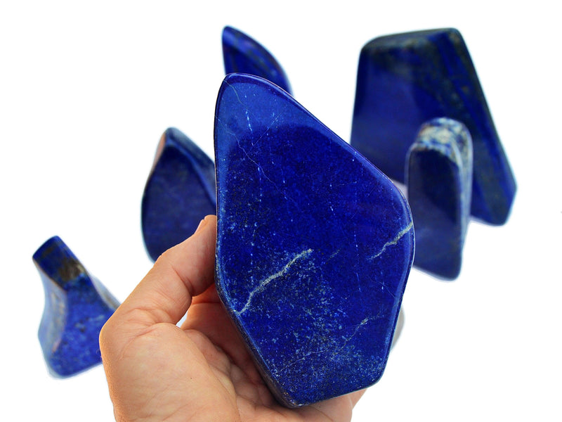 Blue lapis free form slab crystal 130mm on hand with background with some stones on white