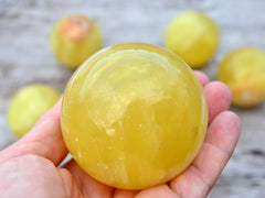 One lemon yellow calcite sphere crystal 60mm on hand with background with some stones on wood table