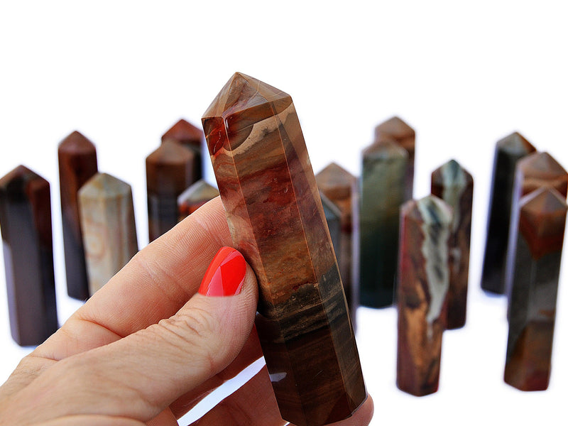 One polychrome jasper crystal point 90mm on hand with background with some towers on white