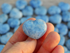 One blue calcite mini crystal heart 30mm on hand with background with several heart stones on wood table