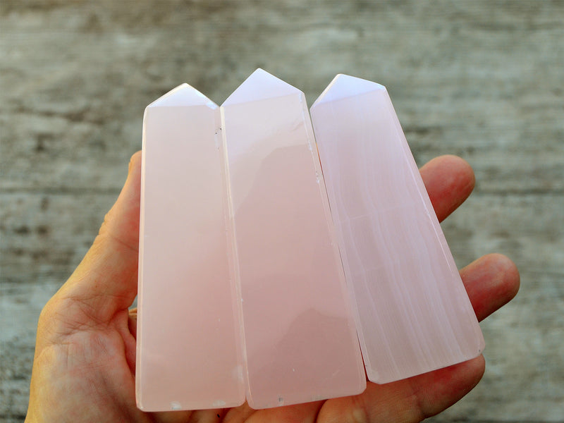 Three pink mangano calcite obelisks 85mm on hand with white background