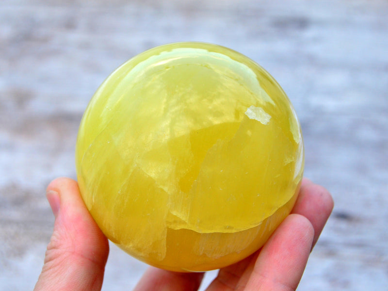 One lemon yellow calcite ball 65mm on hand with wood background