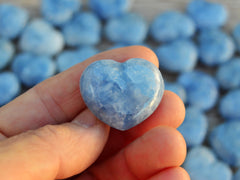 One blue calcite small crystal heart 30mm on hand with background with several heart stones on wood table