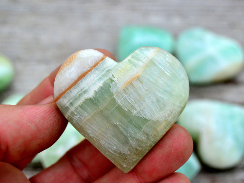 One green banded pistachio calcite hart mineral 40mm on hand with background with some stones on wood table