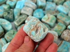 One blue aragonite cube tumbled crystal on hand with background with several stones