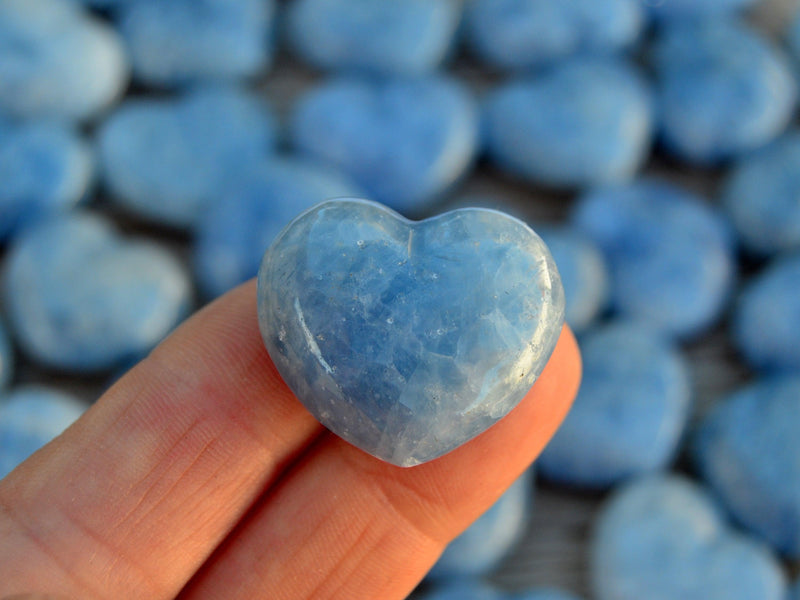 One blue calcite mini heart 30mm on hand with background with several heart stones on wood table