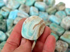 On blue aragonite cube tumbled stone 25mm on hand with background with several crystals