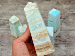 One large caribbean calcite crystal obelisk 130mm on hand with background with some crystals on wood table
