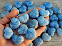 Ten small blue calcite hearts 30mm on hand with background with some crystals on wood table