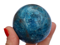 One blue apatite sphere crystal 50mm on hand with white background