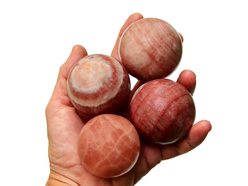 Four rose calcite spheres 50mm on hand with white background