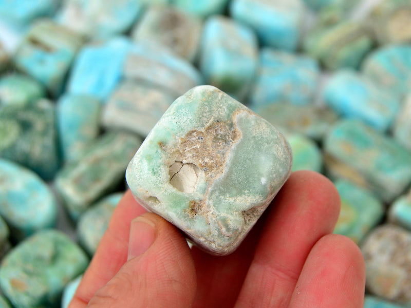 One blue aragonite cube tumbled mineral on hand 30mm with background with several stones