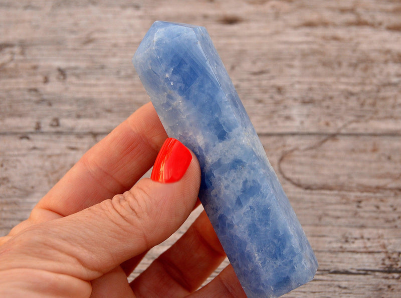 One blue calcite tower 90mm on hand with wood background