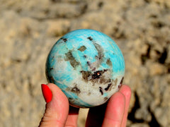 One green amazonite ball 65mm on hand with rock background