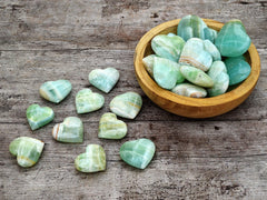 Several pistachio calcite heart shapped crystals 40mm-80mm inside a wood bowl with background with some hearts on wood table