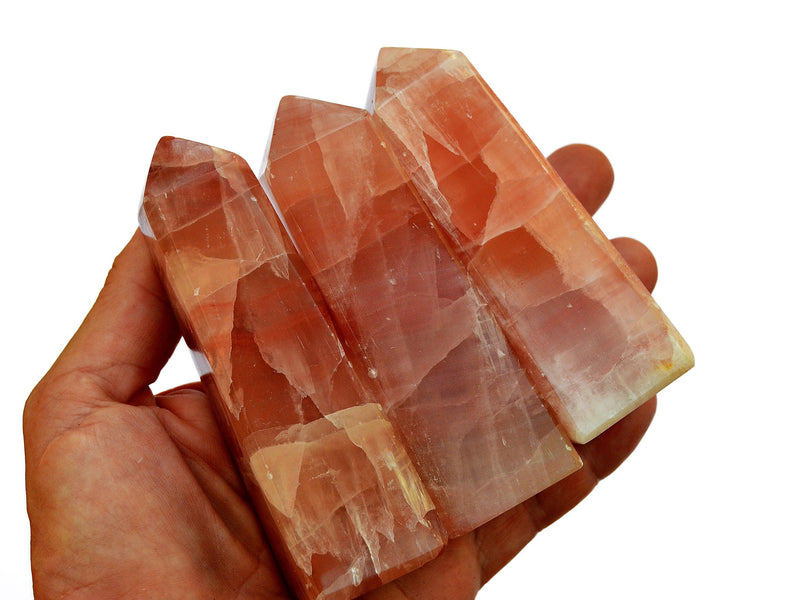 Three pink calcite crystal obelisks 80mm-85mm on hand with white background