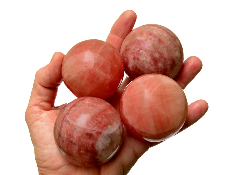 Four rose calcite sphere crystals 50mm on hand with white background