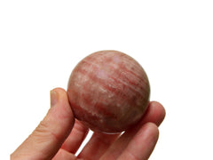 One rose calcite sphere crystal 50mm on hand with white background