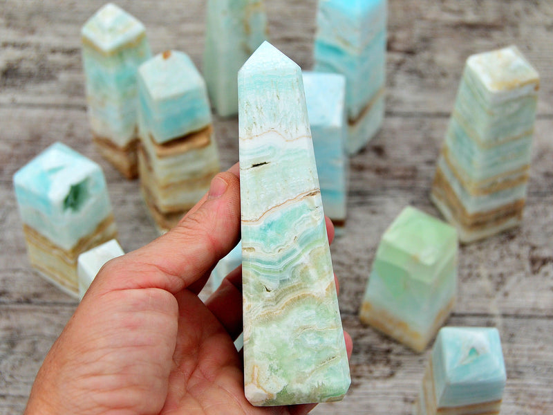 One caribbean calcite crystal obelisk on hand with background with some crystals on wood table