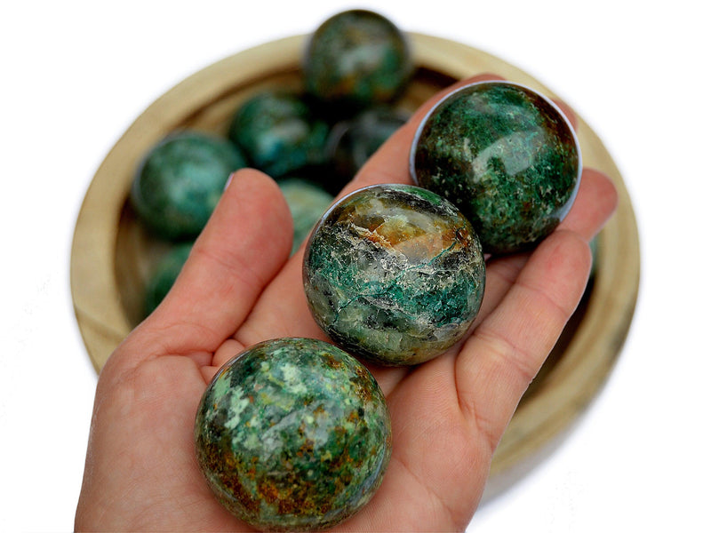 Three green chrysocolla sphere stones 40mm on hand with background with some balls inside a wood bowl