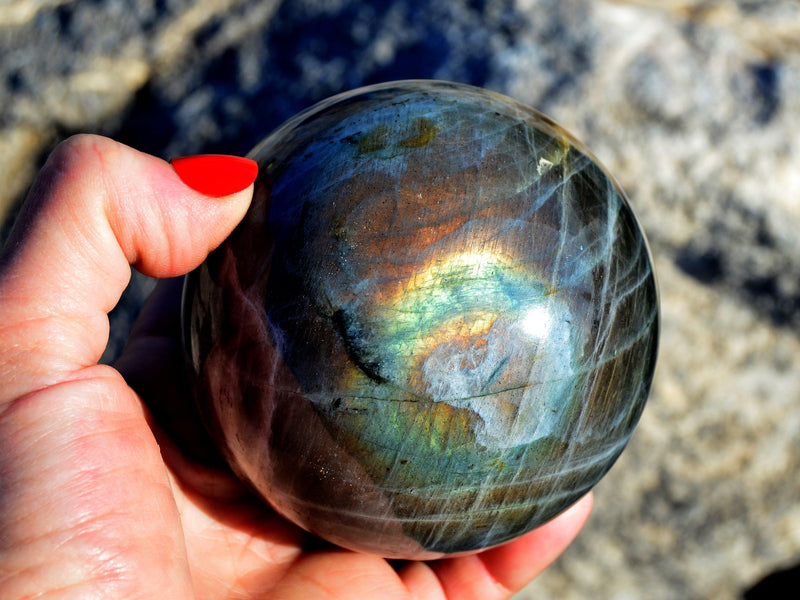 One large labradorite sphere 80mm on hand with rock background
