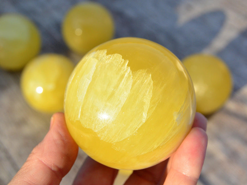 One lemon yellow calcite ball 65mm on hand with some stones on wood table