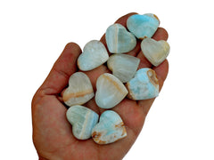 Ten small blue green caribbean calcite crystal hearts 25mm-30mm on hand with white background