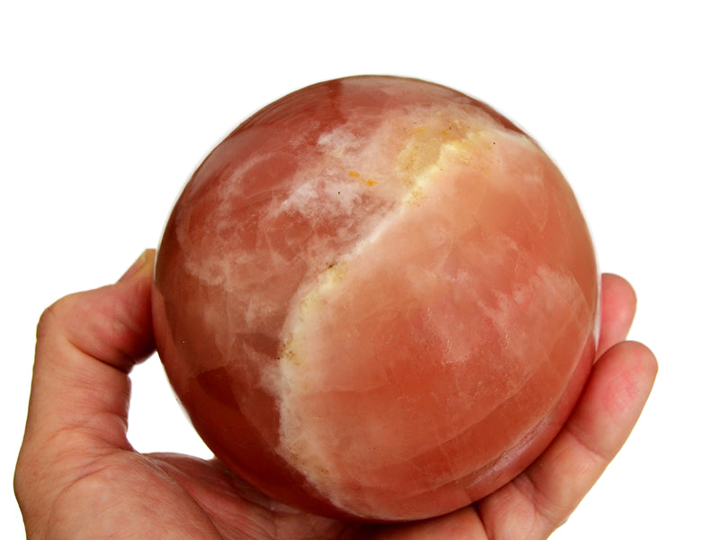 One rose calcite crystal sphere 85mm on hand with white background