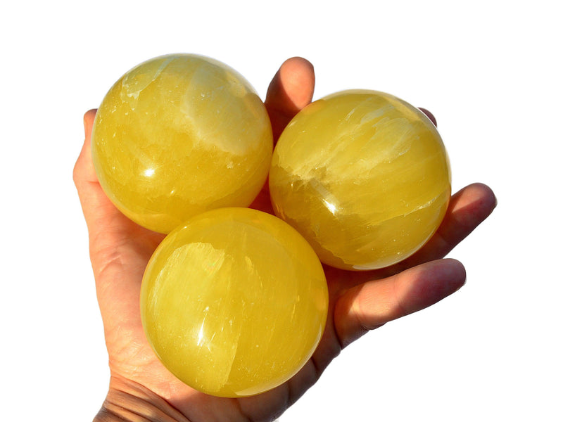 Three lemon calcite spheres 65mm on hand with white background