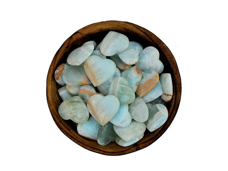 Several small blue green caribbean calcite heart shapped stones inside a wood bowl on white background