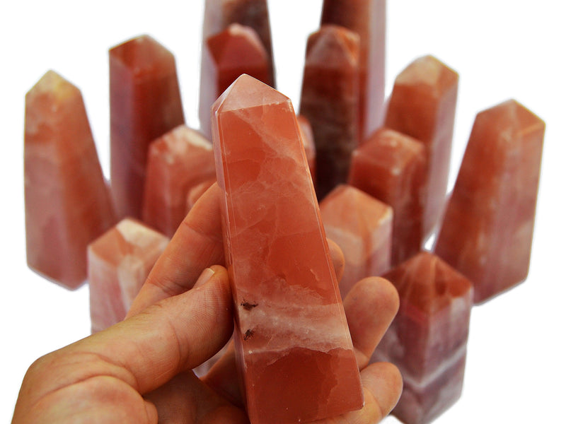 One pink calcite obelisk crystal 90mm on hand with background with some crystals on white