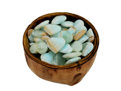 Several blue green caribbean calcite heart shapped minerals inside a wood bowl on white background