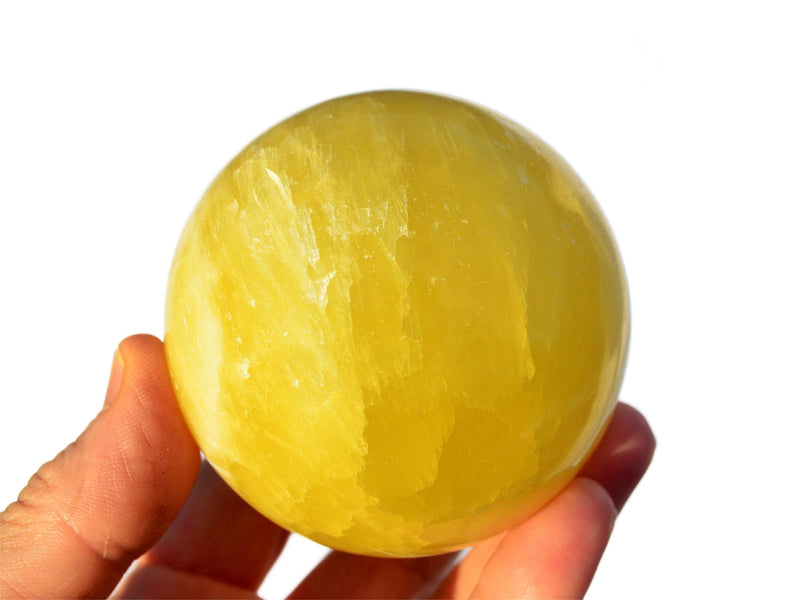 One large lemon calcite sphere crystal 60mm on hand with white background
