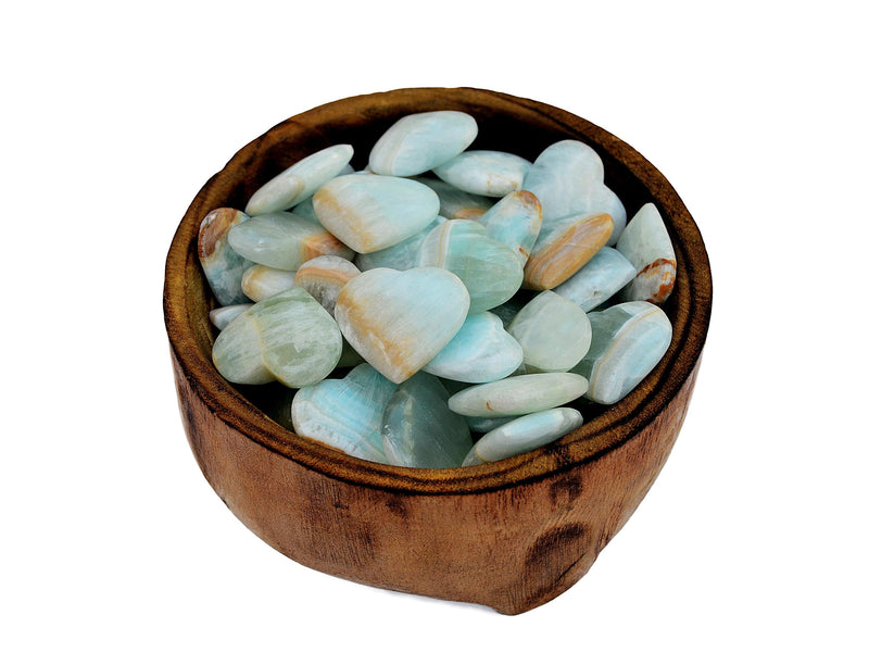 Several blue green caribbean calcite heart shapped minerals inside a wood bowl on white background