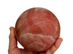 One rose calcite crystal sphere 90mm on hand with white background