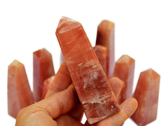 One  pink calcite crystal tower 90mm on hand with background with some obelisks on white