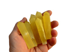 Some small yellow calcite faceted crystal points 50mm-65mm on hand with white background
