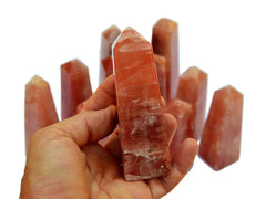 One rose calcite obelisk crystal 80mm on hand with background with some crystals on white