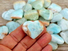 One small caribbean calcite heart crystal on hand with background with some hearts on wood table