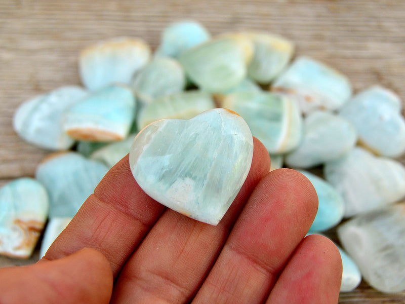 One small blue caribbean crystal heart 25mm on hand with background with some hearts on wood table