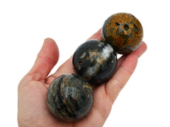 Three green and mustard yellow ocean jasper spheres 45mm on hand with white background